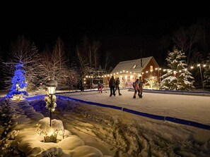 Un espacio exterior cubierto de nieve con un edificio, un árbol de Navidad azul iluminado y personas caminando.