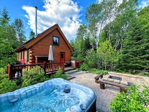 Una cabaña de madera con jacuzzi y zona de estar exterior rodeada de árboles.