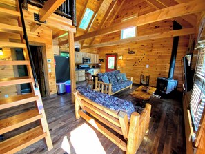 Interior acogedor de una cabaña con piso de madera, un sofá, una mesa de comedor, una zona de cocina y una escalera que lleva a un nivel superior.