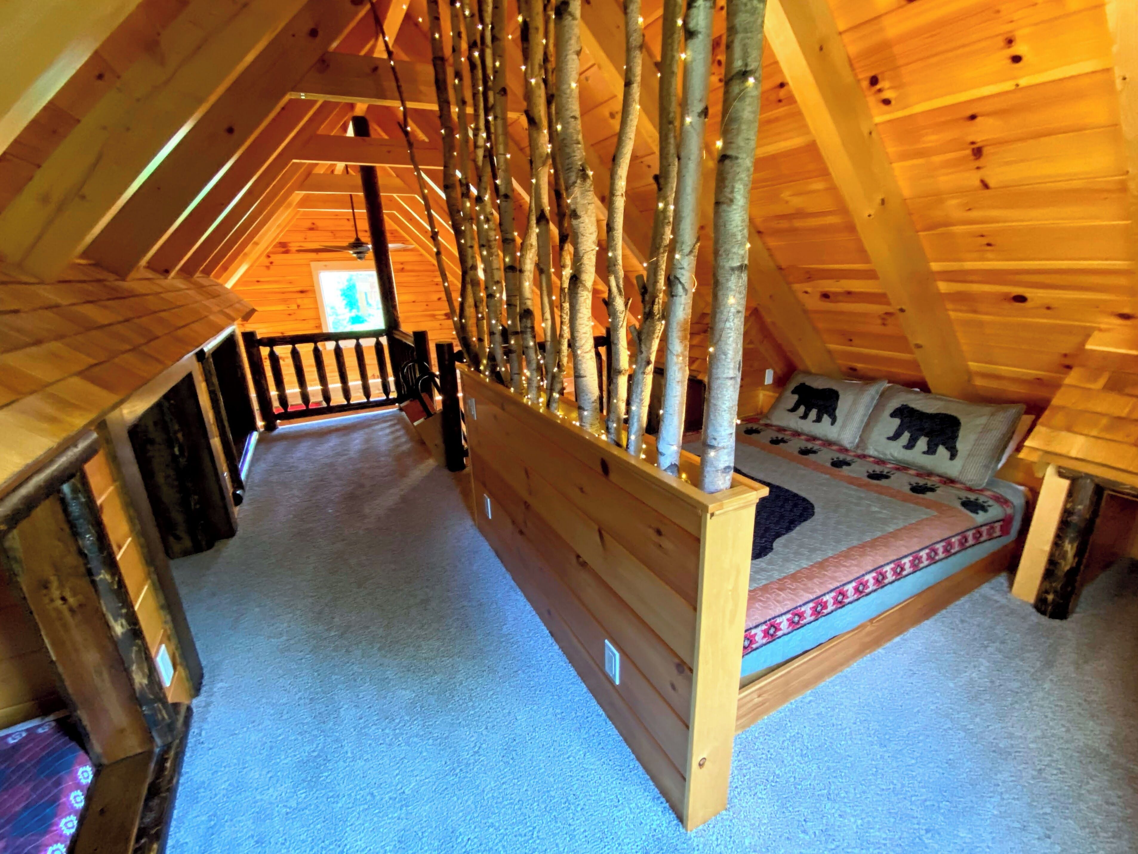 A cozy attic bedroom with a wooden bunk bed, a small window, and a wooden railing.