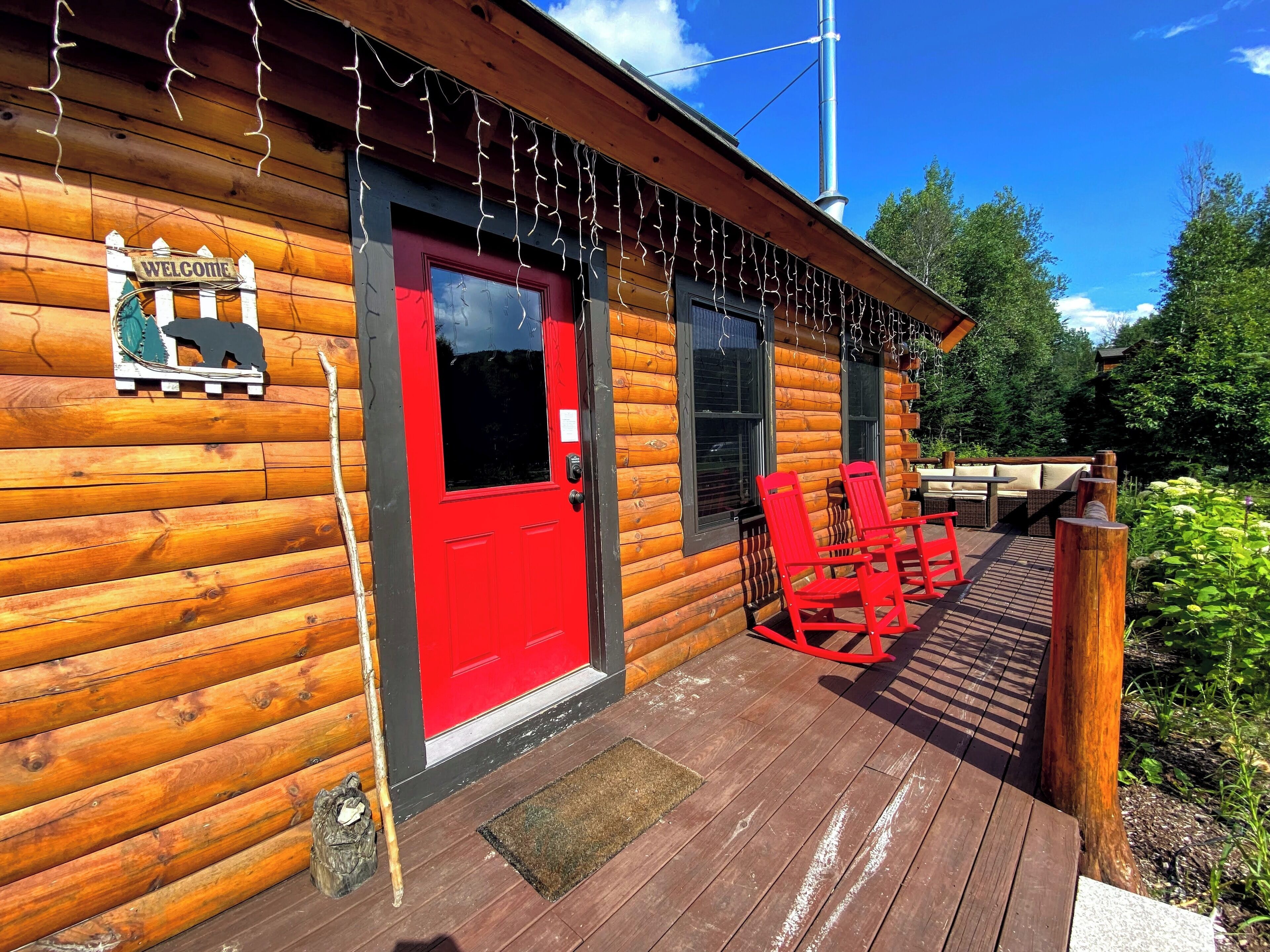Una cabaña de troncos con una puerta roja, un letrero de bienvenida y un adorno decorativo con la silueta de un oso.