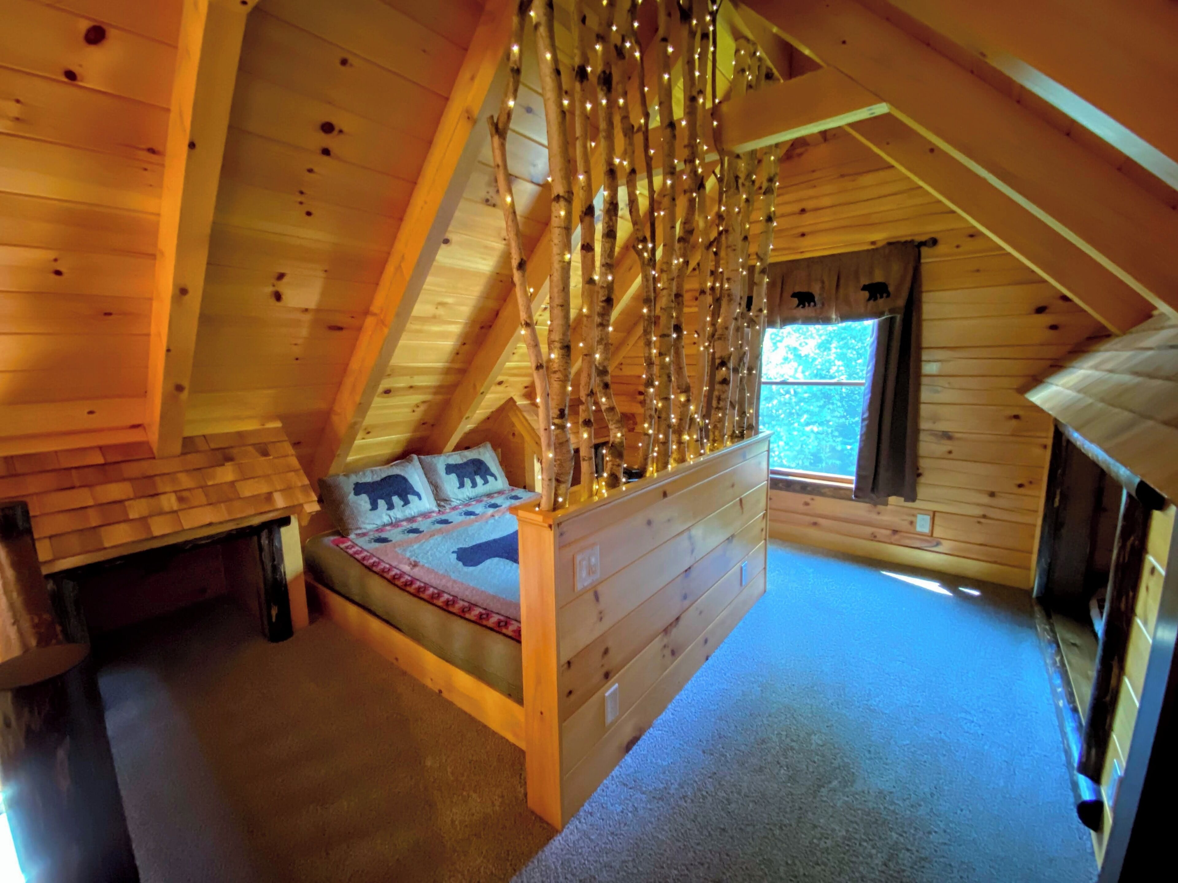 A cozy attic bedroom with a wooden bed, a nightstand, and a window with a view of the outdoors.