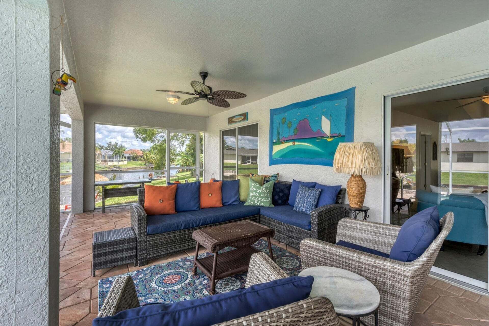 A covered patio with wicker furniture, a ceiling fan, and a painting of a landscape.