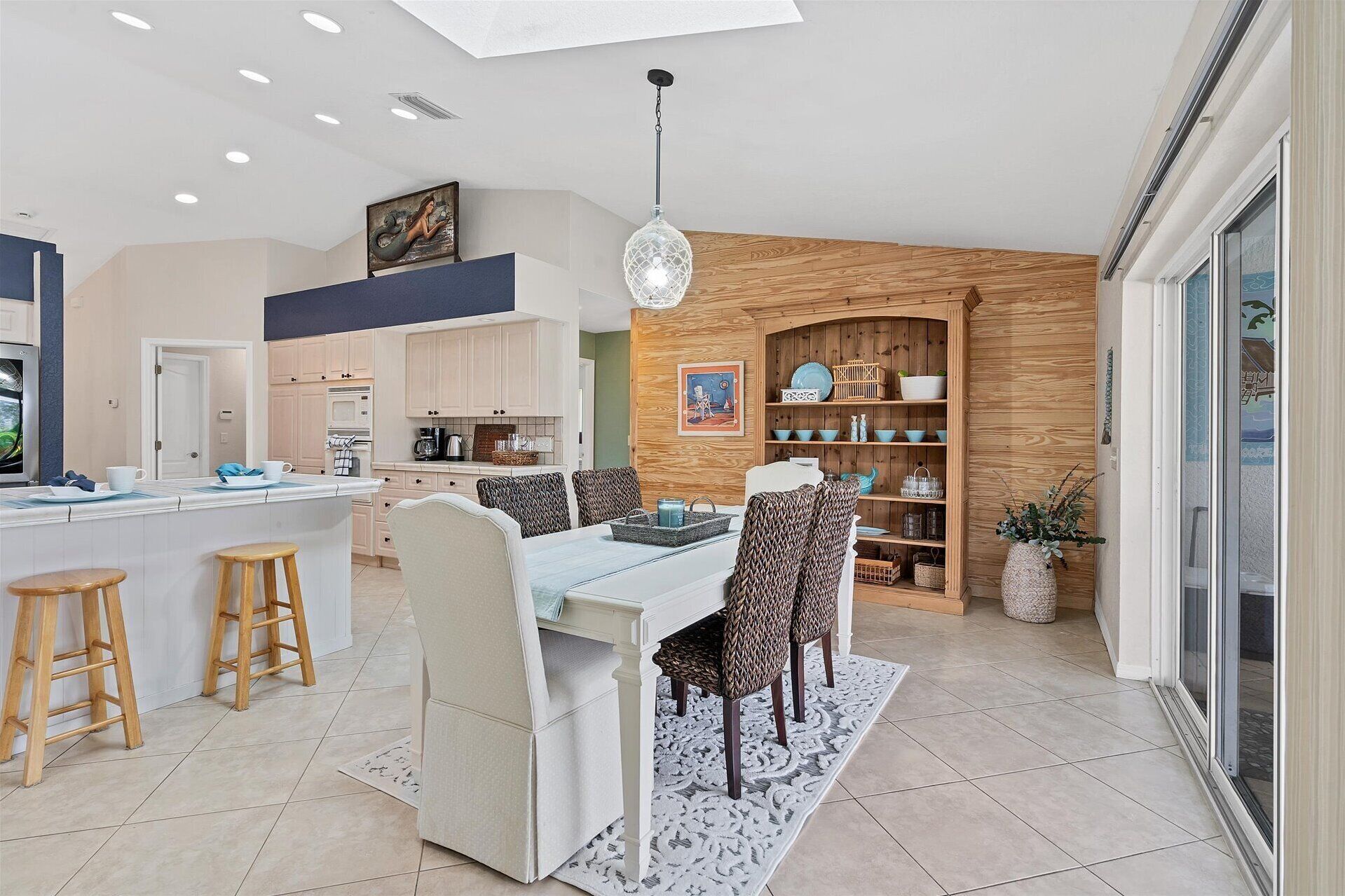 A modern kitchen with a central island, wooden cabinetry, and a dining area with a white table and patterned chairs.