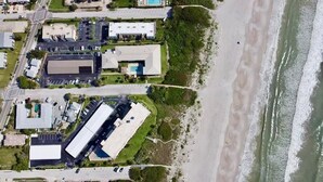 Vue aérienne d’une propriété située sur la côte, comprenant plusieurs bâtiments, un parking et une plage.