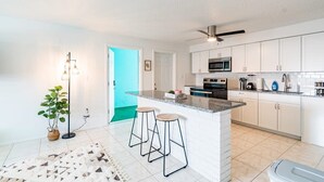 Une cuisine moderne avec des meubles blancs, un plan de travail en granit et un îlot central doté de tabourets.