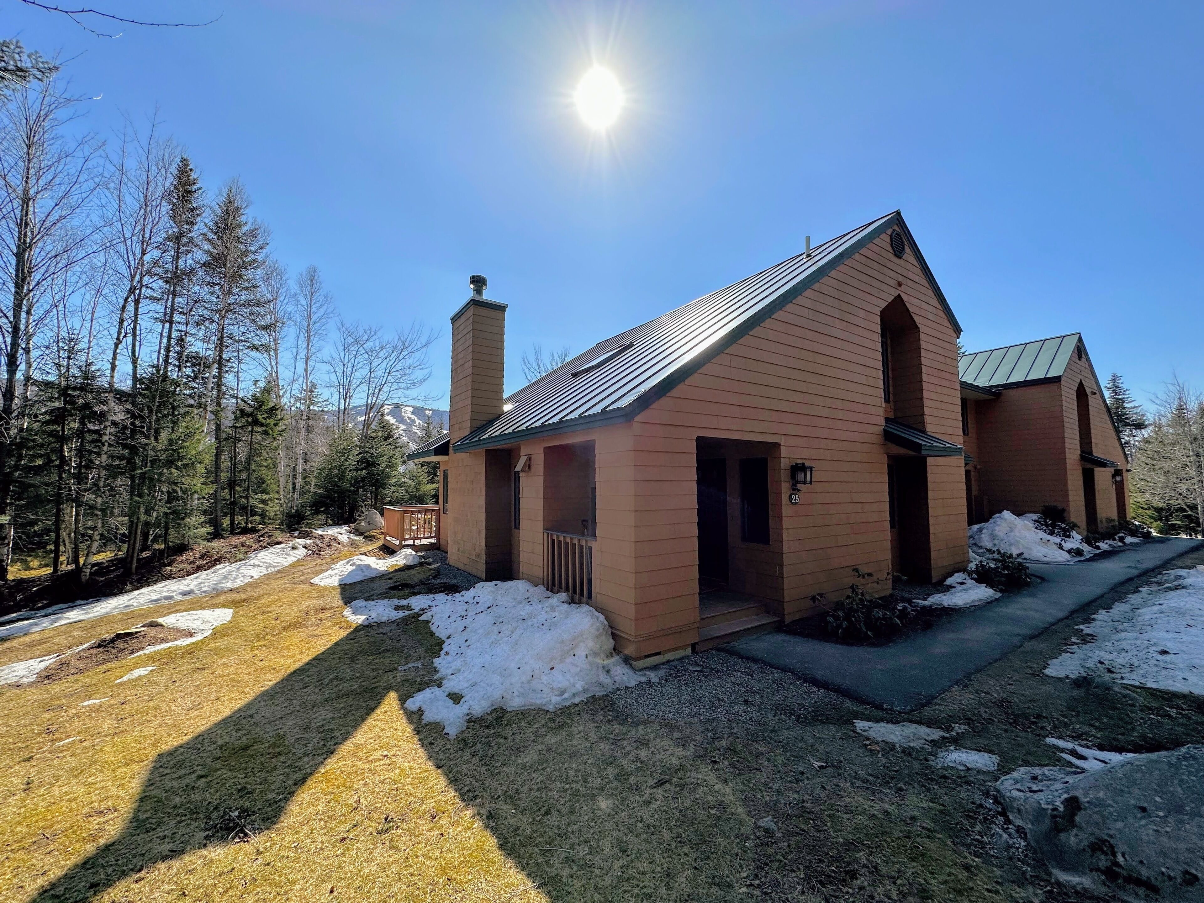 A two-story wooden cabin with a chimney, a deck, and a snow-covered yard.