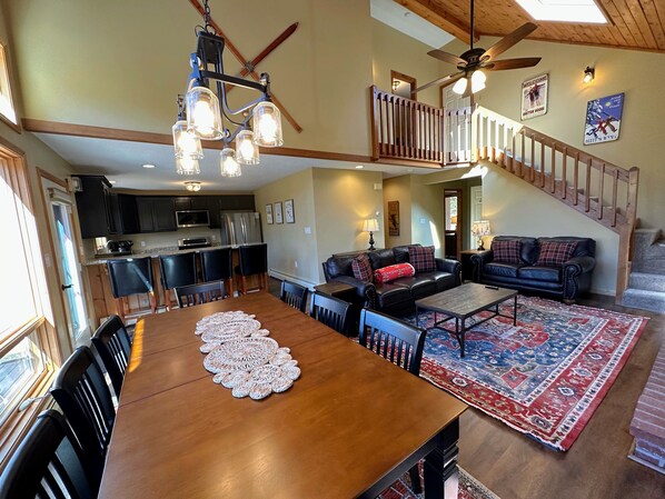 A spacious living area with a wooden dining table, a black leather sofa, and a red patterned rug.