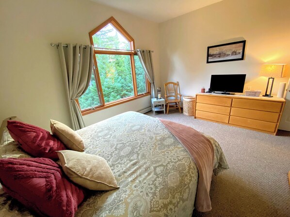 Une chambre à coucher avec un grand lit, une commode en bois, un téléviseur et une fenêtre avec des rideaux.