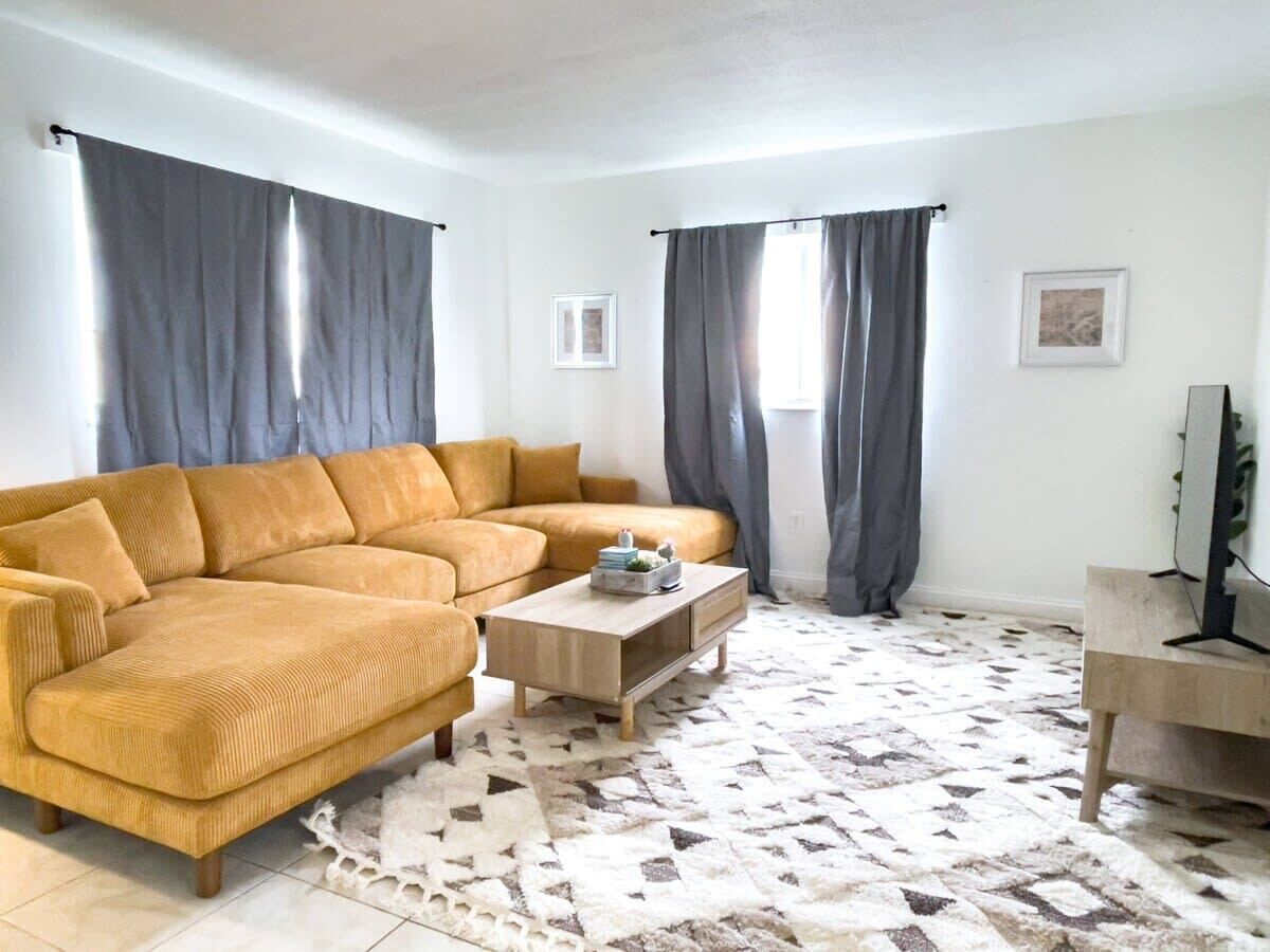 A living room with a mustard-colored sofa, a wooden coffee table, and a patterned rug.