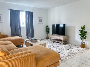 A living room with a sofa set, a coffee table, a TV stand, and a patterned rug. - Fillmore Unit 1 (Cape Canaveral)