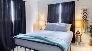 Une chambre à coucher bien rangée, avec un lit, deux lampes de chevet, un luminaire fixé au mur et une plante en pot.