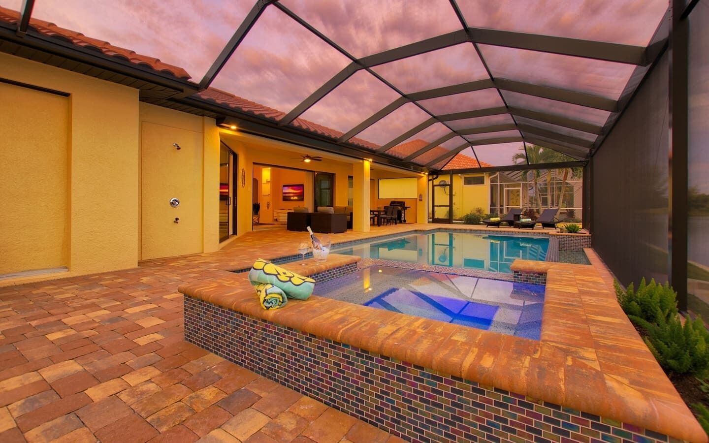 A swimming pool with a tiled deck, a covered patio area, and a view of the surrounding landscape.