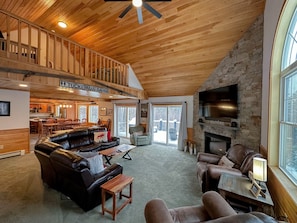 A spacious living area with a high ceiling, a stone fireplace, and a balcony overlooking a snowy landscape. - Hl96 Single Family Home With Views and Lots of Space! Privacy, Convenience, AC and Style! (Bretton Woods)