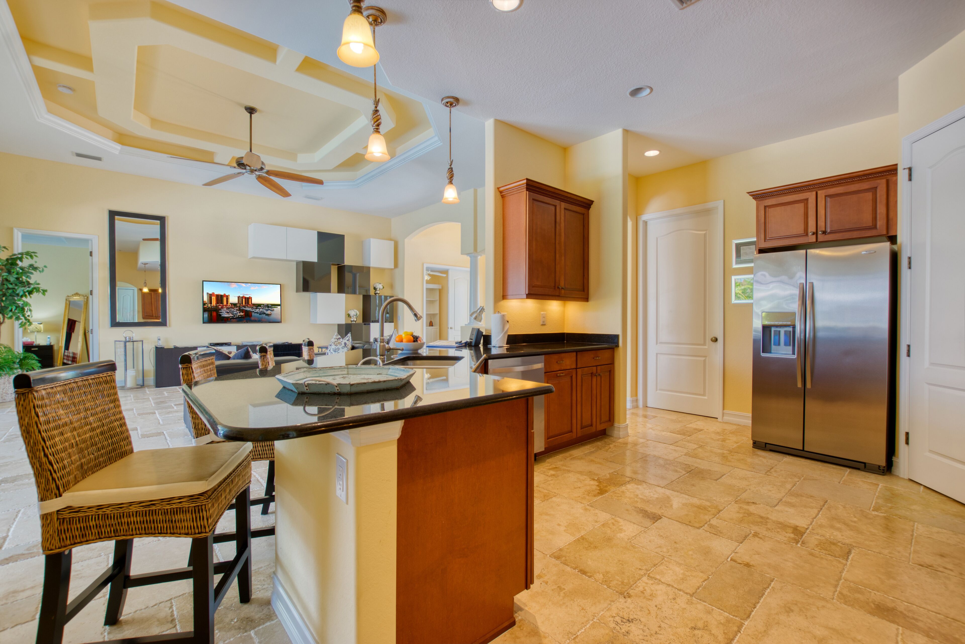A spacious kitchen with a large island, wooden cabinets, a stainless steel refrigerator, and a ceiling fan.
