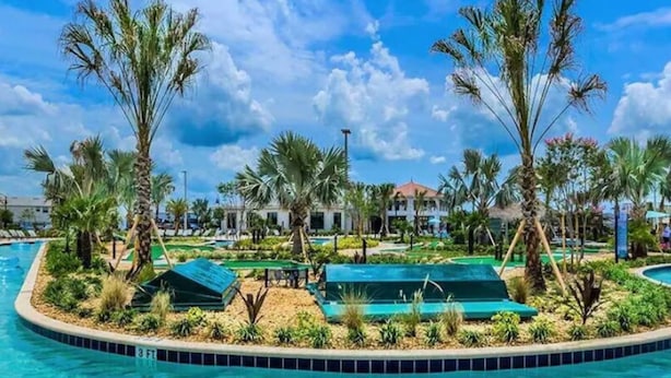A pool area with palm trees, lounge chairs, and a building in the background. - 4BR Disney 15 min Pool Resort Access (Kissimmee)