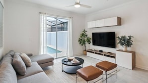 A modern living room with a sofa, coffee table, and TV stand. - 4BR Disney 15 min Pool Resort Access (Kissimmee)