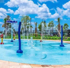 Una piscina con múltiples chorros de agua y un cielo azul despejado.