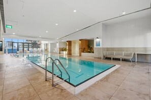 Ein großer, überdachter Swimmingpool mit klarem Wasser, umgeben von gefliestem Boden und einer Bank an der Wand.