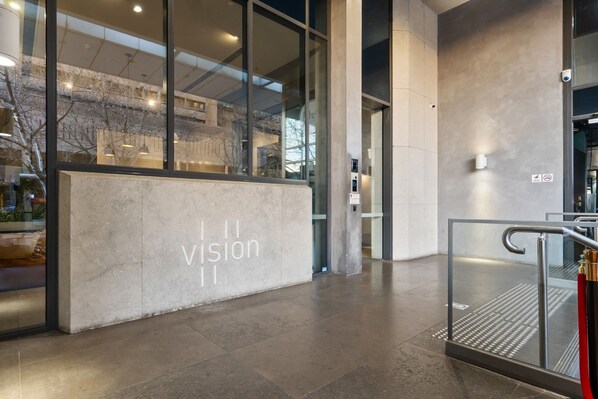 Ein moderner Gebäudeeingang mit Glasfassade, einem Betonschreibtisch und einer Metalltreppe.