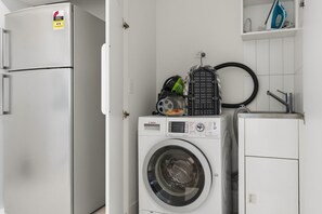 Eine kleine Küche mit Waschmaschine, Kühlschrank und einer Ablage für Reinigungsmittel.