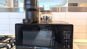 Un microondas negro con pantalla digital, una cafetera y un tarro de nueces encima.
