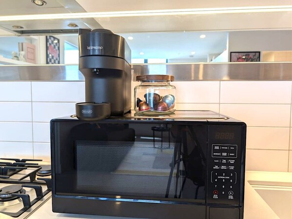 A black microwave oven with a digital display, a coffee maker, and a jar of nuts on top. - Boutique Eclectic City Apt | Pool, Sauna & Carpark (Melbourne)