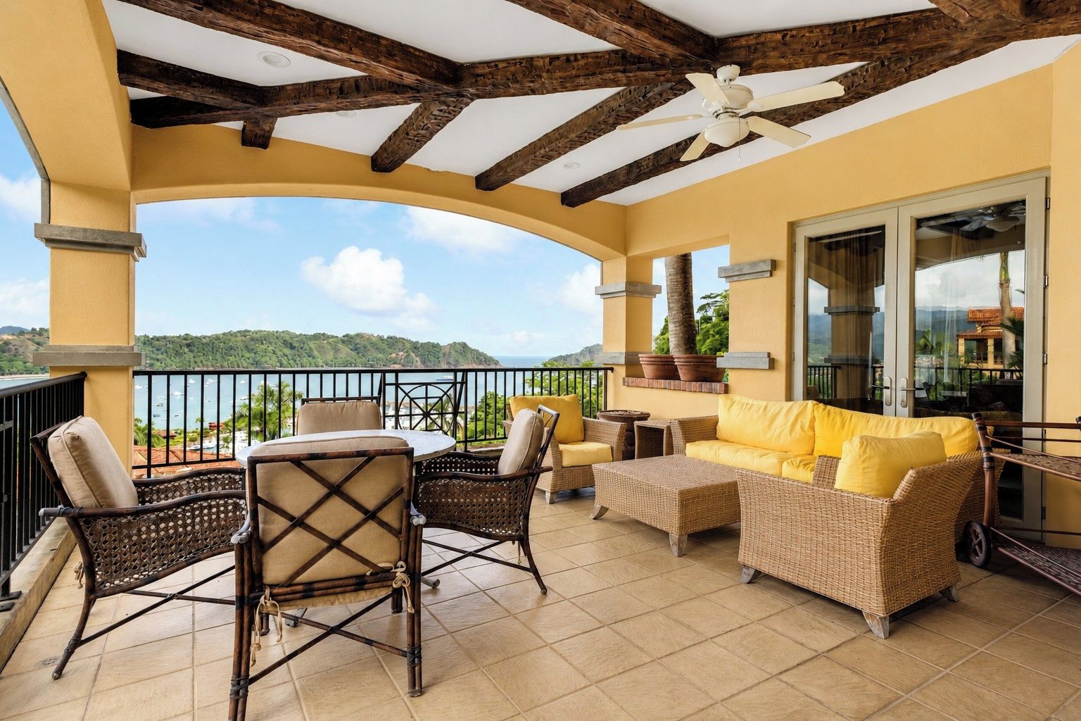A balcony with wicker furniture, a ceiling fan, and a view of the sea.