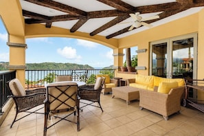 A balcony with wicker furniture, a ceiling fan, and a view of the sea.