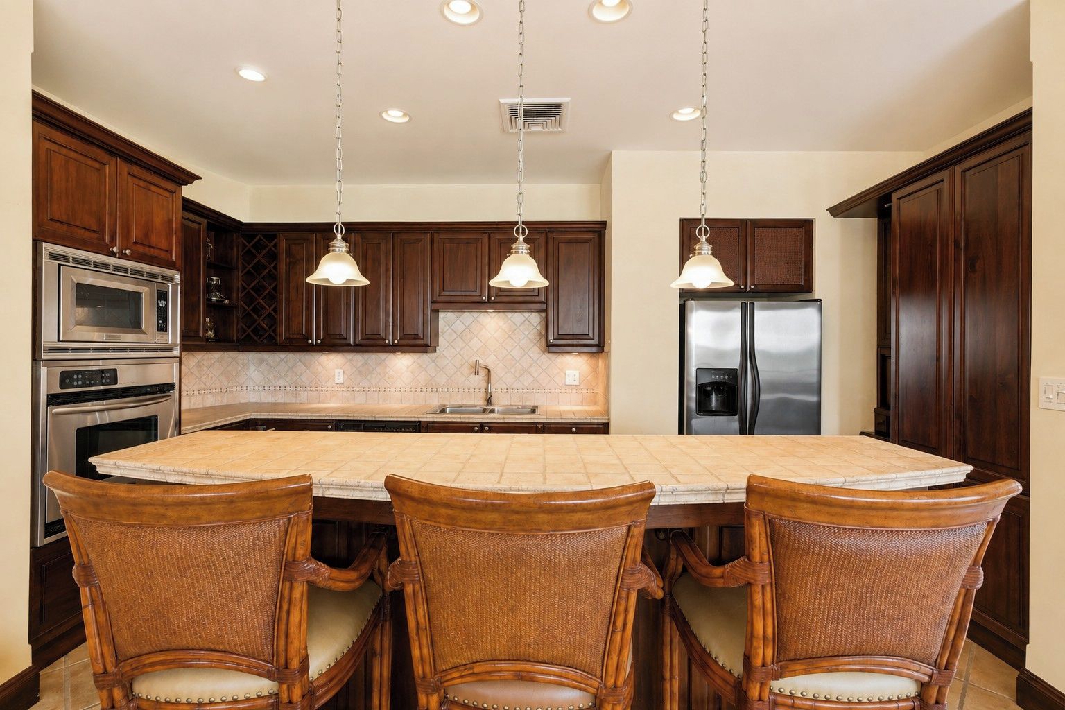 A kitchen with a central island, wooden cabinets, stainless steel appliances, and pendant lighting.