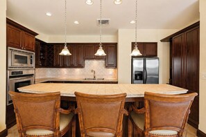 A kitchen with a central island, wooden cabinets, stainless steel appliances, and pendant lighting.