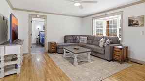 A living room with a sofa, coffee table, TV, and a ceiling fan. - Lazy Bear Meadow | Dog-Friendly Cabin with Fenced Yard, Hot Tub & Putting Green (Sevierville)