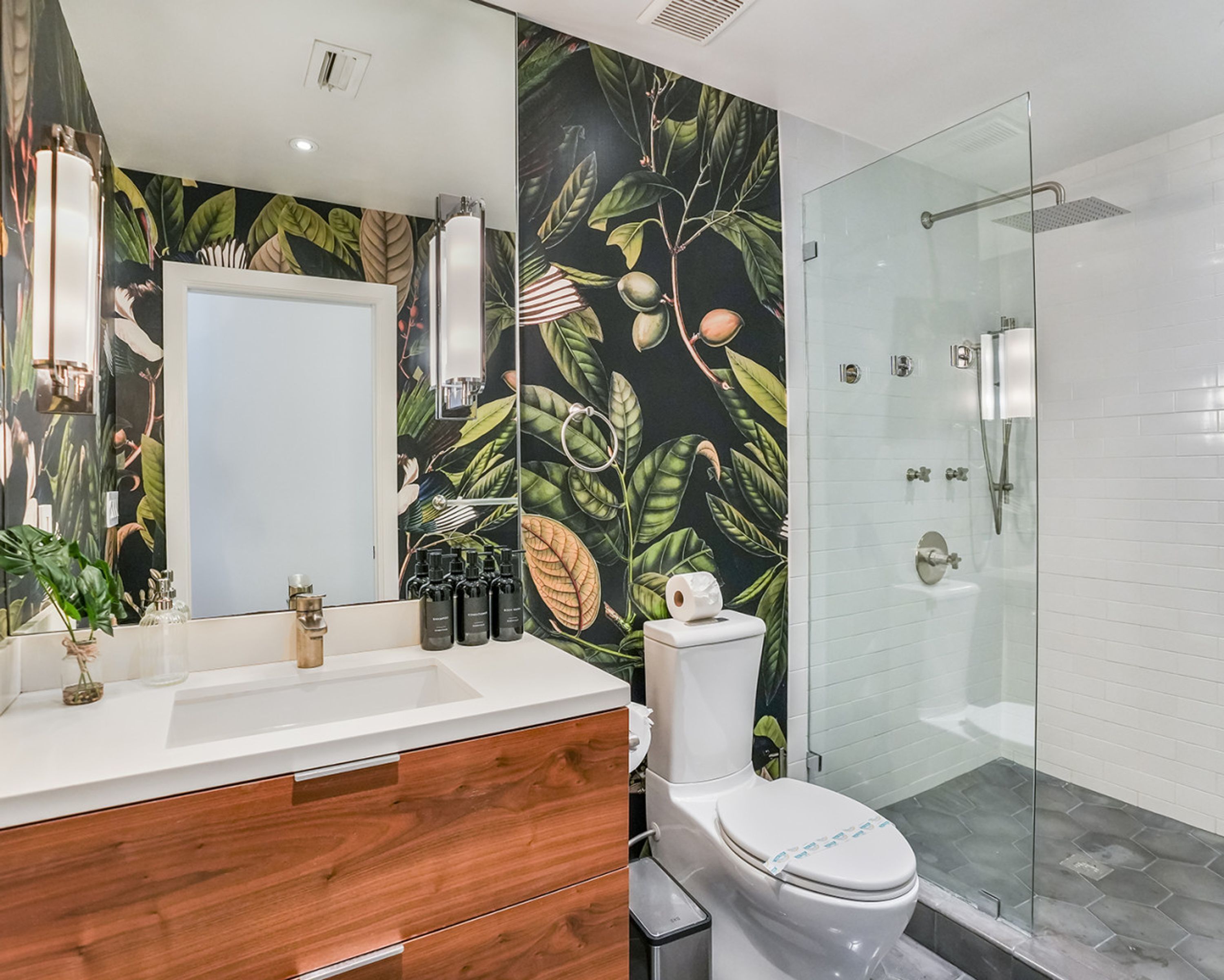 Een badkamer met een witte wastafel, een houten wastafelmeubel, een toilet en een douchecabine van glas.