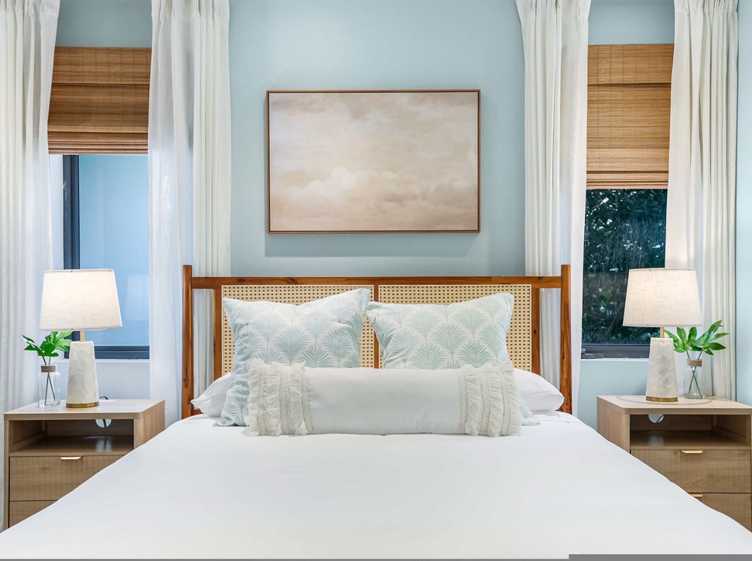 Un dormitorio ordenado con una cama grande, dos mesitas de noche con lámparas y una obra de arte enmarcada en la pared.