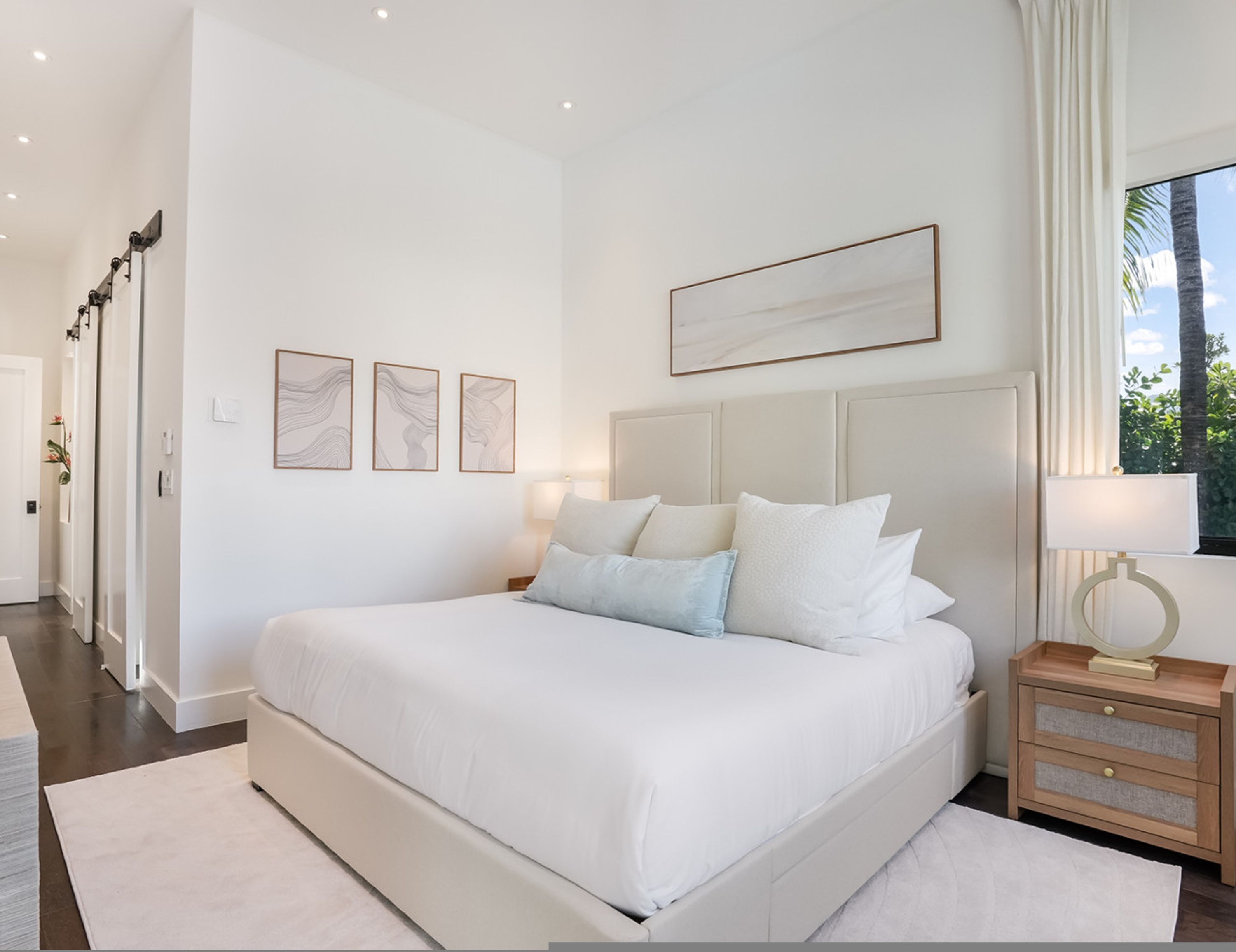 Un dormitorio espacioso con una cama grande, una mesita de noche y una ventana con vista a palmeras.