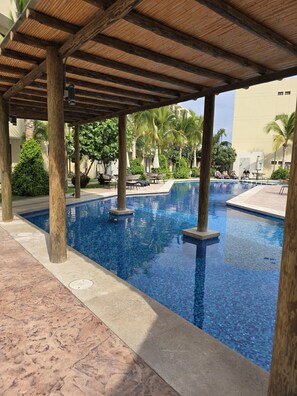 A pool area with a wooden pergola, lounge chairs, and palm trees. - Our paradise designed to make you feel  at home, but with the luxury (Mazatlán)
