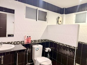 Ένα μπάνιο με λευκό νιπτήρα, τουαλέτα και χώρο για ντους. Στον πάγκο του νιπτήρα υπάρχουν διάφορα είδη προσωπικής υγιεινής.