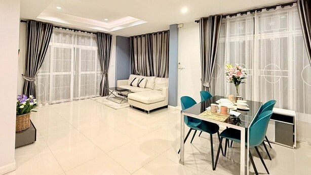 Uma sala de estar moderna com um sofá, uma mesa de jantar com cadeiras e grandes janelas com cortinas.