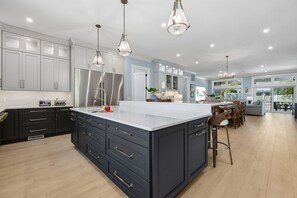 Una cocina moderna con una isla grande, muebles oscuros, electrodomésticos de acero inoxidable, iluminación colgante y un comedor con vistas.