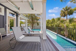 Un área de piscina techada con sillones de descanso, piscina y vista a un barrio residencial.
