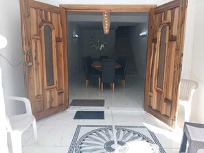 A wooden door leading to a dining area with a chandelier, a tiled floor with a decorative pattern, and a staircase in the background. - Cambridge Heights Guest House (Port Maria)