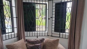 A corner sofa with a brown cushion and a window with metal bars.