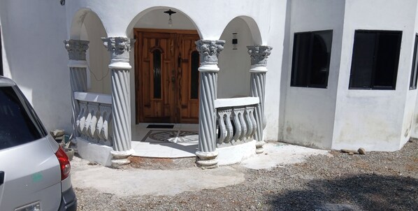 A building with a wooden door, white columns, and a gravel driveway. - Cambridge Heights Guest House (Port Maria)
