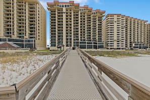 A boardwalk leading to a beachfront with high-rise buildings in the background. - Gorgeous 2BR Beachfront Condo - Phoenix II Resort #2062 (Orange Beach)