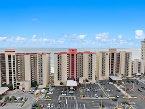 A high-rise hotel with multiple floors, a parking lot in front, and a view of the ocean. - Gorgeous 2BR Beachfront Condo - Phoenix II Resort #2062 (Orange Beach)