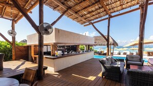 An outdoor bar area with a pool view, wooden deck, and wicker furniture. - Ocean Breeze: New downtown room (Isla Mujeres)