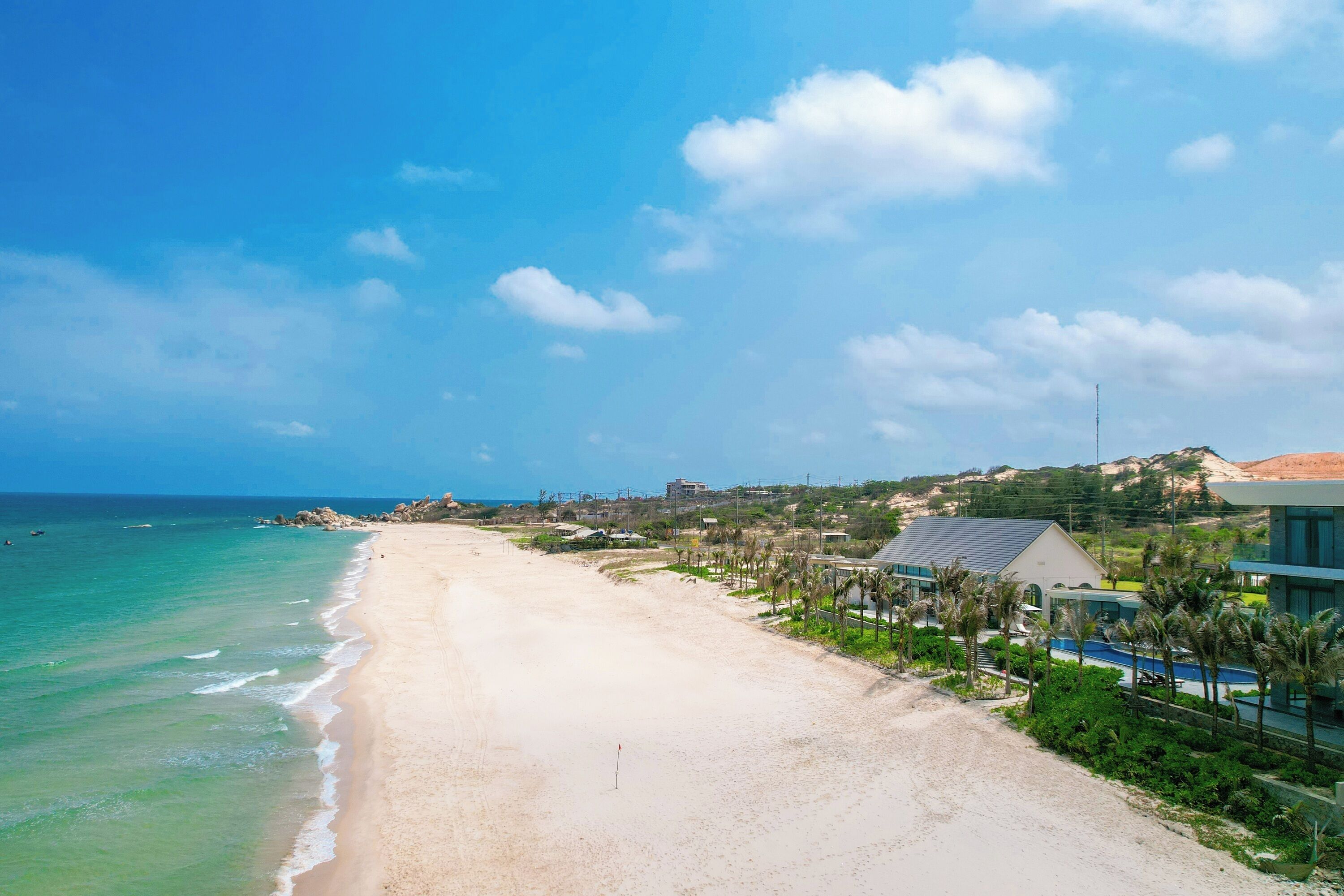 A beach with a clear sky, a sandy shore, and buildings in the background.