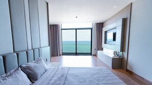 Une chambre d’hôtel moderne dotée d’un grand lit, d’un téléviseur fixé au mur et offrant une vue sur l’océan par une grande fenêtre.