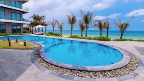 Une piscine à bord incurvé, entourée d’un chemin de galets, de palmiers et offrant une vue sur l’océan.