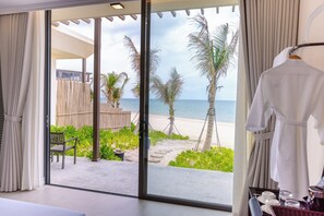 Une chambre dotée d’une grande porte-fenêtre coulissante donnant sur la plage, une robe blanche suspendue à un porte-manteau et une petite table avec un plateau.